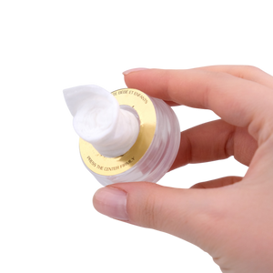 Hand holding a small container of cream with a white lid on a white background