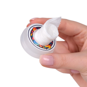 Hand holding a small container of cream with a colorful label on a white background