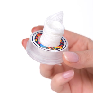 Hand holding a small container with colorful design and white substance on a white background