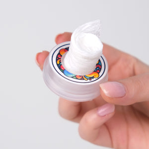 Hand holding a small container with a colorful label on a white background