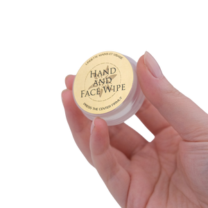 Hand holding a small container of 'Hand and Face Wipe' with a visible label.