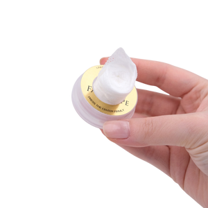 Hand holding a small container of cream with a visible brand name on a white background