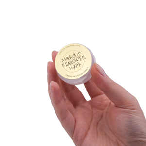 Makeup remover wipe container held in a hand on a white background