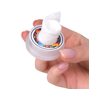 Hand holding a small container with colorful lid design on a white background