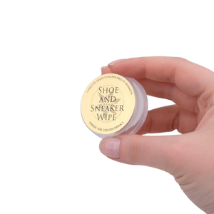 Hand holding a small container labeled 'Shoe and Sneaker Wipe' against a white background