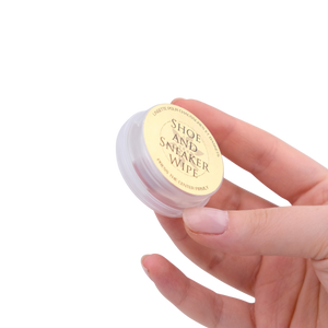 Hand holding a small container labeled 'Shoe and Sneaker Wipe' against a white background