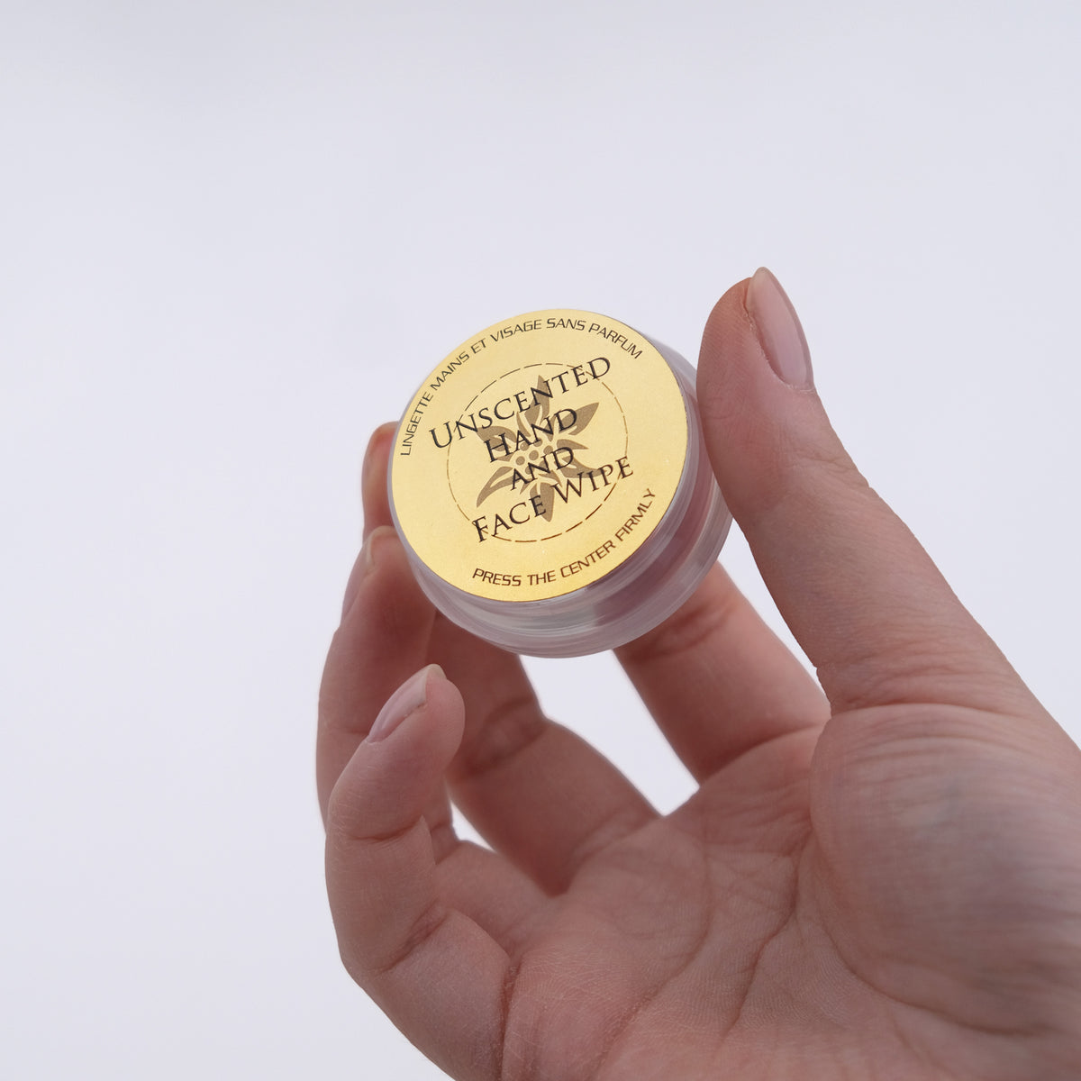 Hand holding a small container of unscented hand and face wipe with a gold lid.