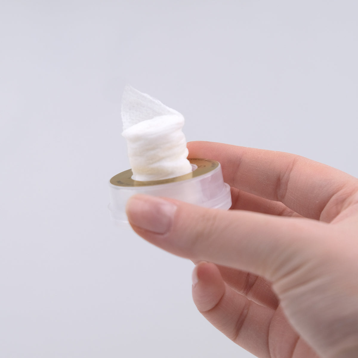 Hand holding a small container of white cream against a light gray background