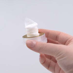 Hand holding a small container of white cream against a light gray background