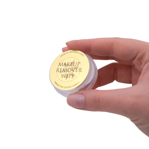 Hand holding a small container of makeup remover wipes on a white background