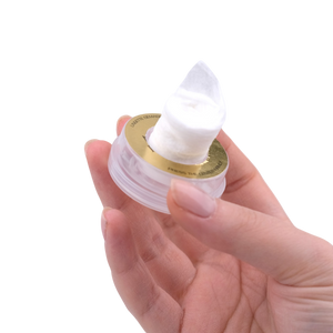 Hand holding a small container of white cream with a gold label on a white background