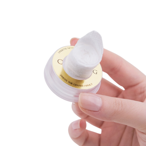 Hand holding a white cosmetic sponge with a gold logo on a white background