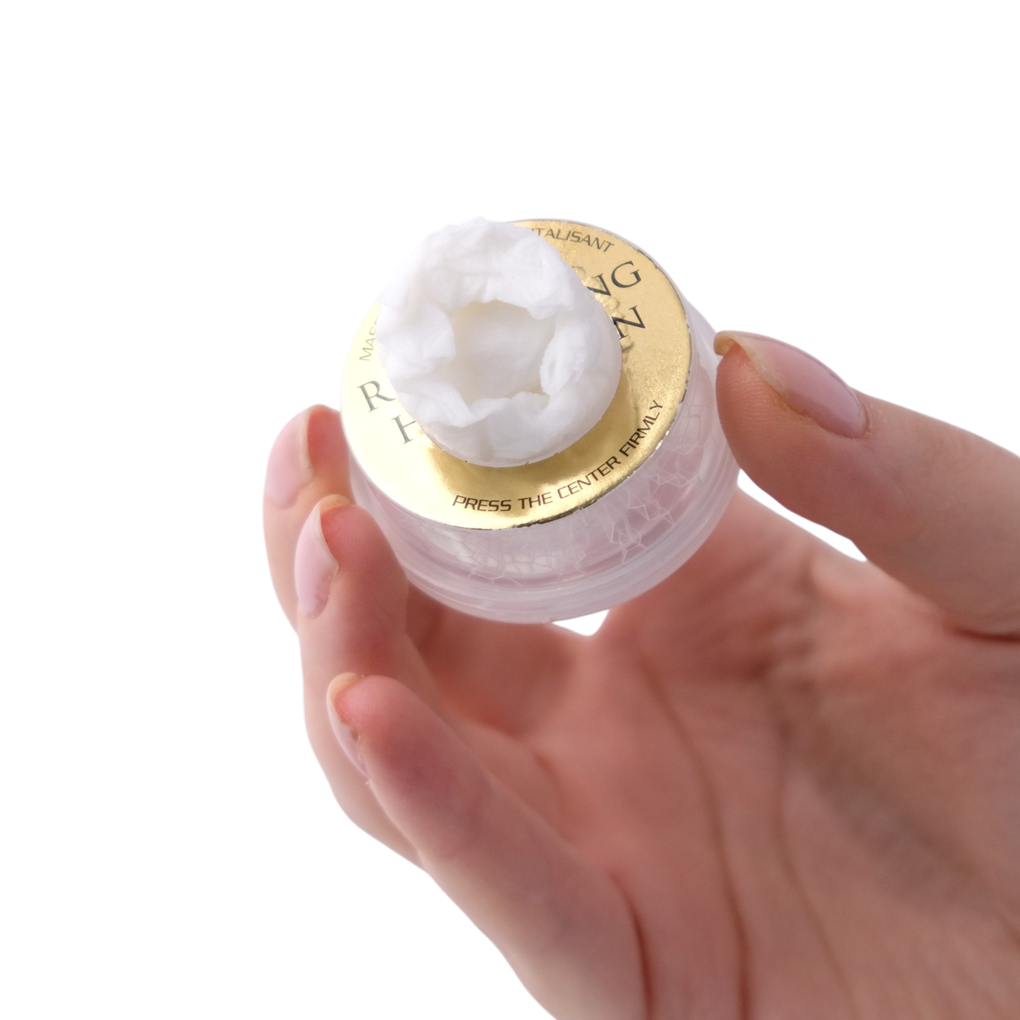 Hand holding a small container of white cream with a gold lid on a white background