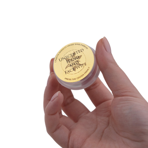 Hand holding a small container of unscented hand and face wipes with a white background
